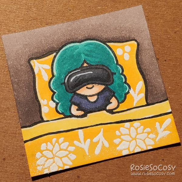 A tiny 2 inch card with a girl sleeping in a bed. She is wearing a black sleeping mask, a very dark bluish grey shirt, and her duvet is a bright yellow with white floral elements.