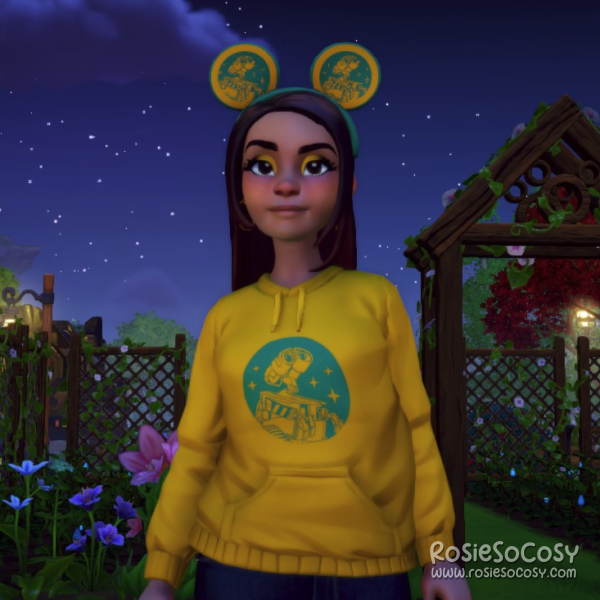 Rosie's avatar in Dreamlight Dreamlight Valley is wearing a yellow hoodie with a teal print of Wall-E, and she has matching Mickey Mouse ears with a yellow/teal Wall-E pattern on them.